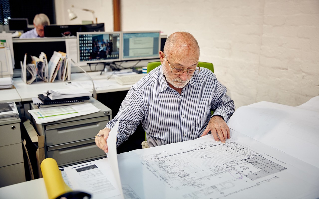 Older man at desk going through paper plans 